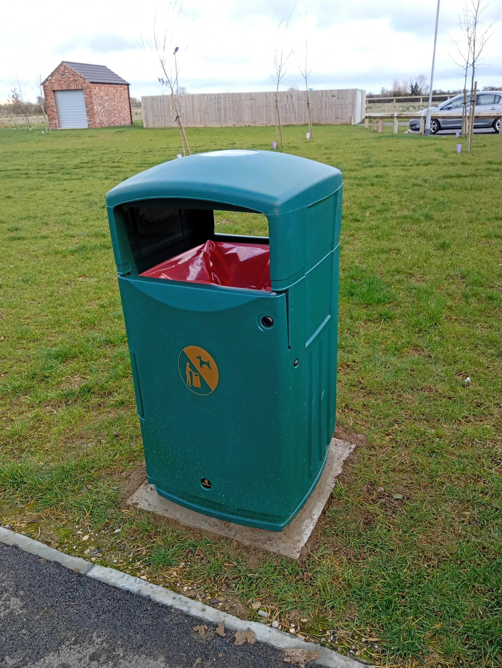 A green litter bin standing on a street, designed for collecting garbage.