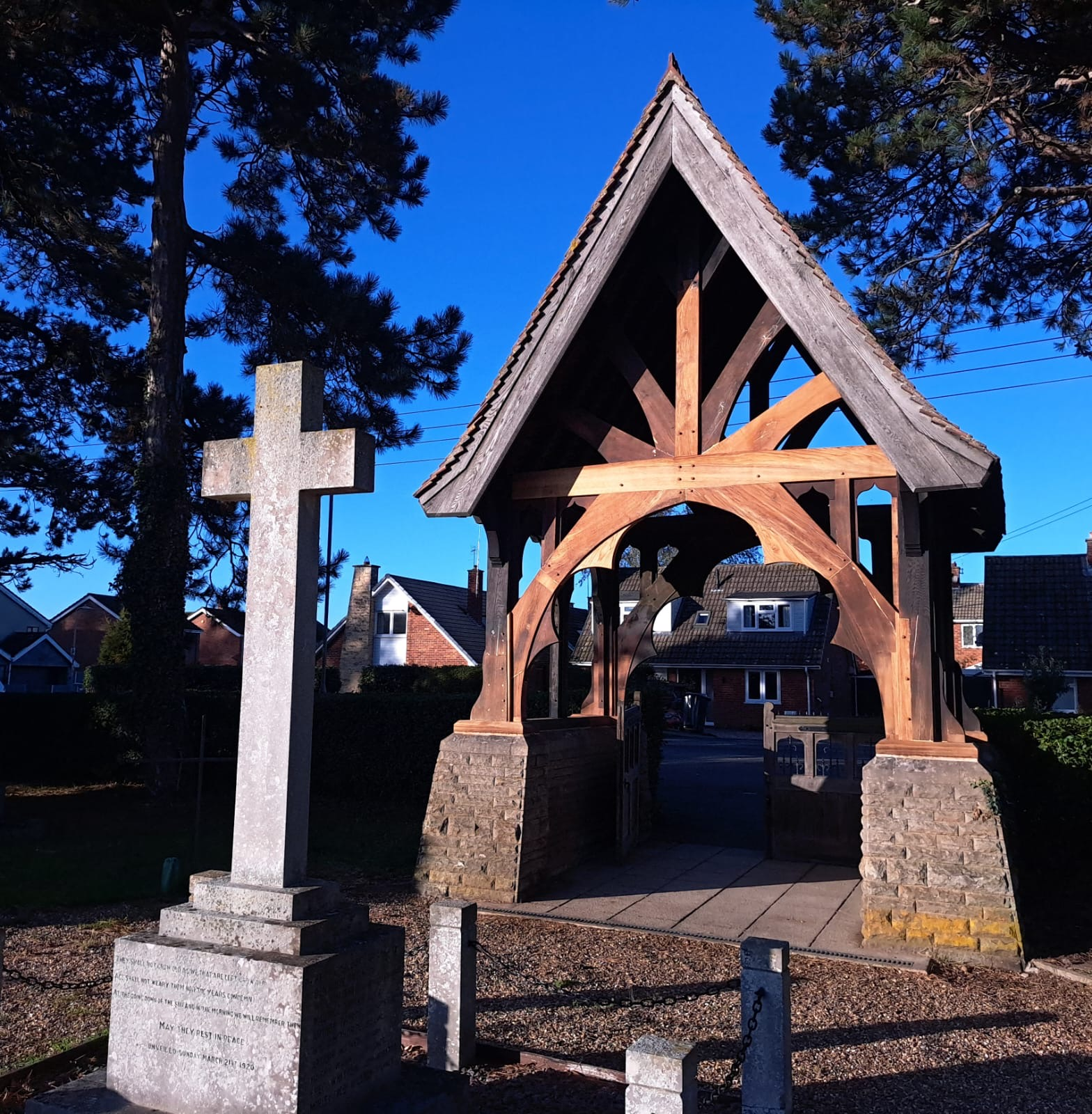 A wooden cross stands beside a gazebo in front of a house, creating a serene outdoor setting.