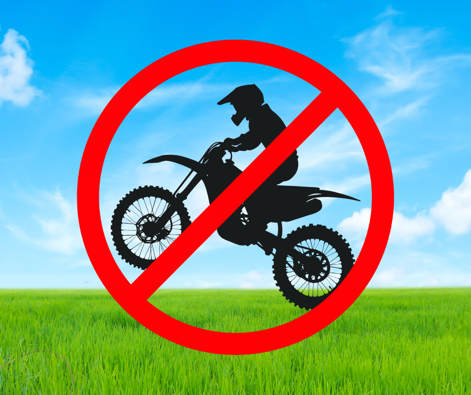 A no motorbike sign stands prominently in a grassy field, indicating the prohibition of motorbike access in the area.