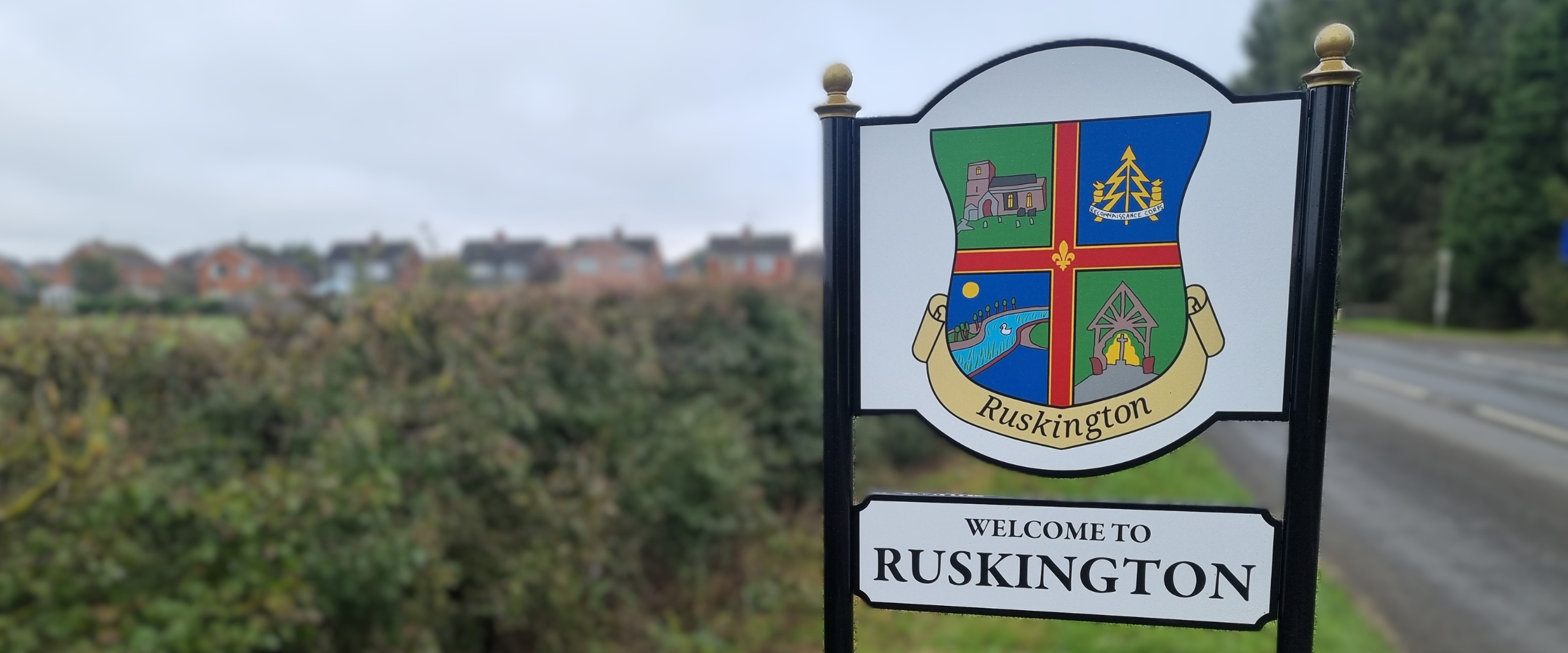 Village sign for Ruskington, showcasing the name in clear lettering, surrounded by greenery and local scenery.